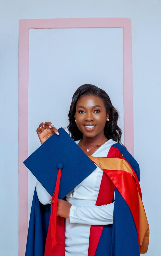Smiling graduate woman holding a blue mortarboard in an academic gown, celebrating success.